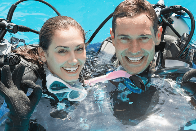 Smiling couple on scuba training in swimming pool showing OK gesture on a sunny day